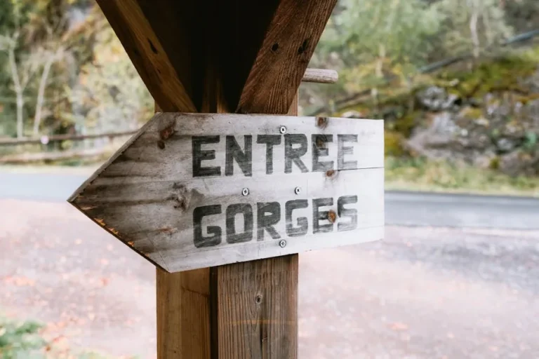 A wooden sign reading 'ENTREE GORGES' outdoors, indicating a gorge entrance.