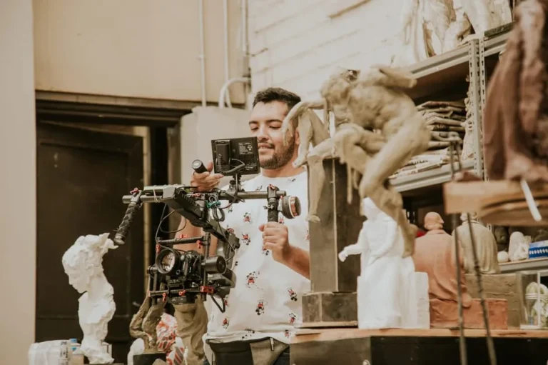 A man using a video camera to capture art sculptures in a studio setting.