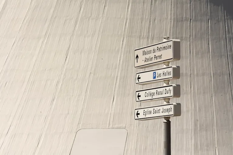 Directional signs in a cityscape setting with modern architectural backdrop.