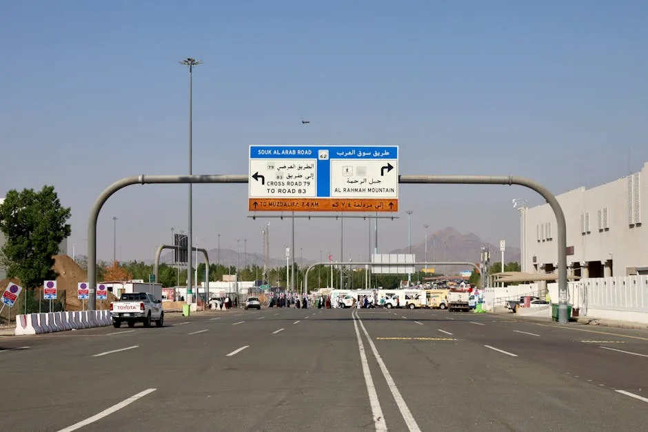 Road signage leading to Al Rahmah Mountain, Mecca, with vehicles and people on a sunny day.