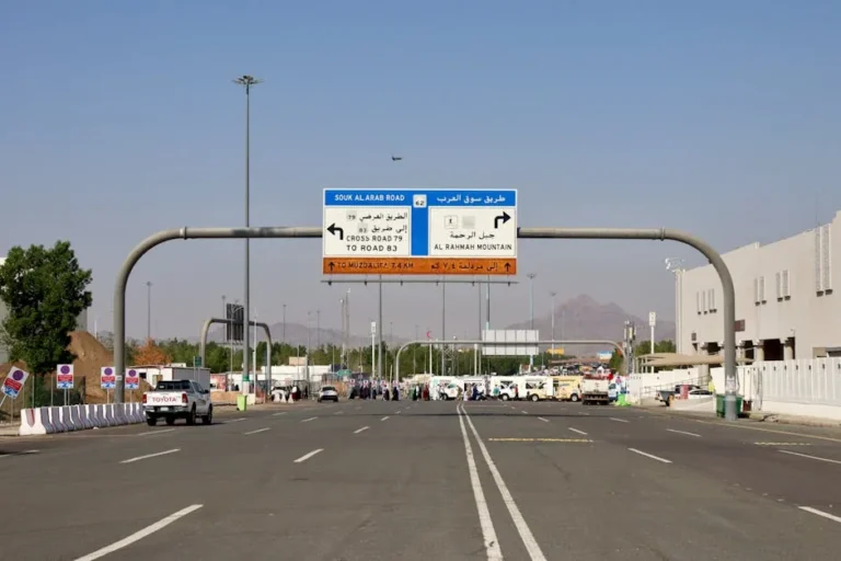 Road signage leading to Al Rahmah Mountain, Mecca, with vehicles and people on a sunny day.
