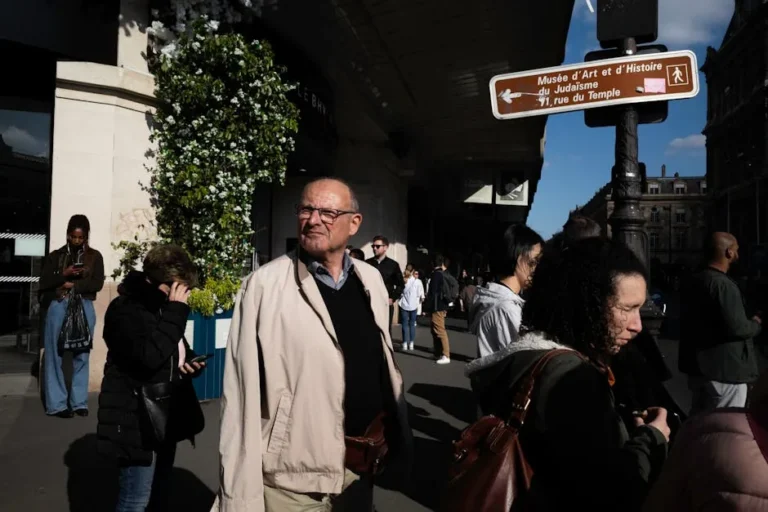 A candid street scene in Paris showing pedestrians and direction signage under bright daylight.